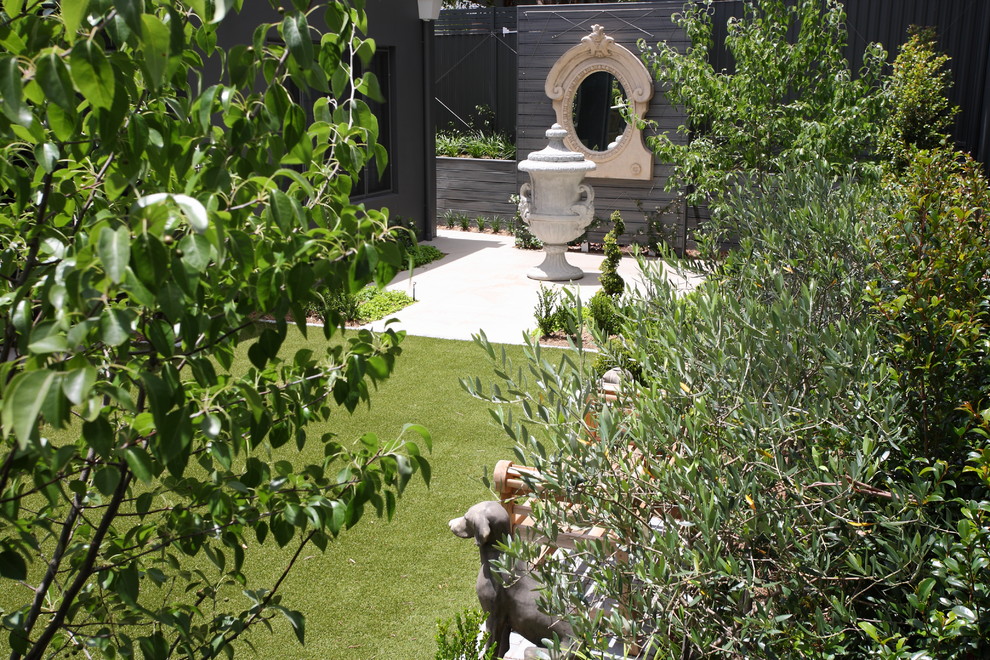 Modern inredning av en mellanstor formell trädgård i full sol framför huset, med naturstensplattor och en fontän