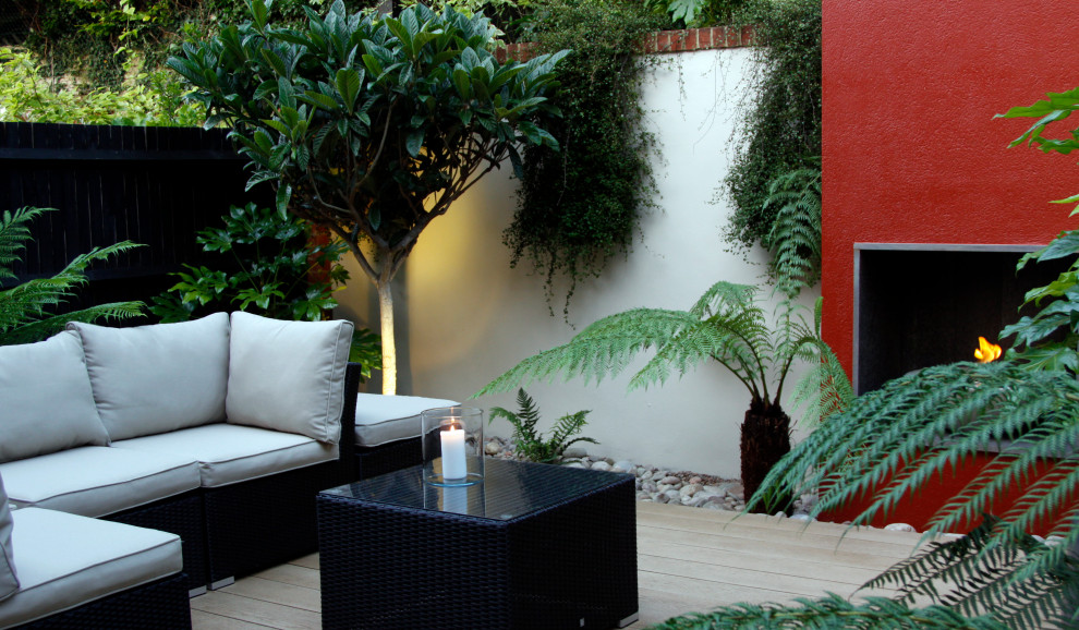 Foto de jardín moderno pequeño en patio trasero con jardín francés, chimenea, exposición parcial al sol y entablado