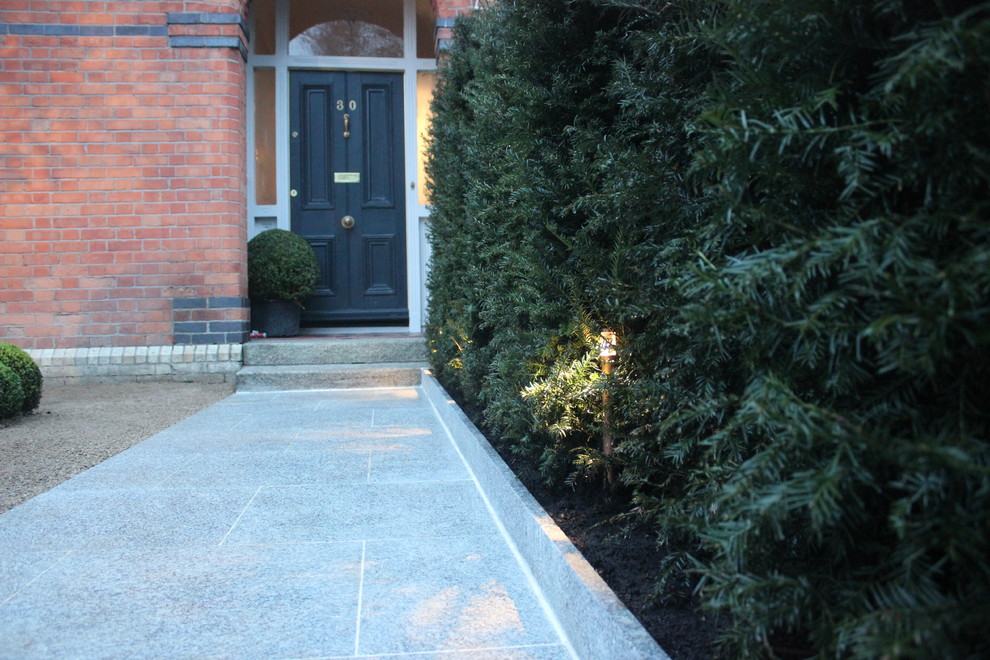 Small victorian front formal full sun garden for summer in Dublin with a garden path and natural stone paving.