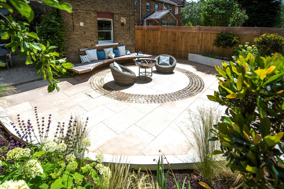 Large trendy backyard stone patio photo in London with a fire pit