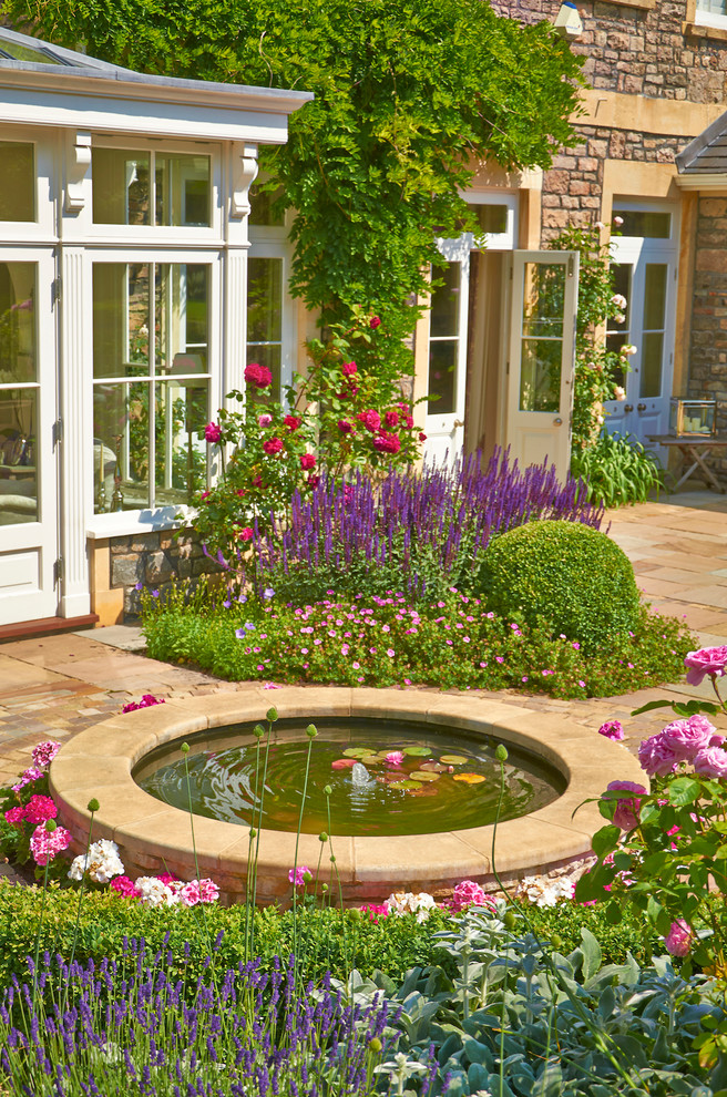 Aménagement d'un jardin arrière classique au printemps avec un point d'eau et une exposition ensoleillée.