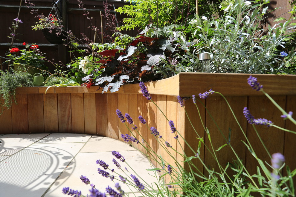 This is an example of a small modern back formal full sun garden in London with a fire feature and natural stone paving.