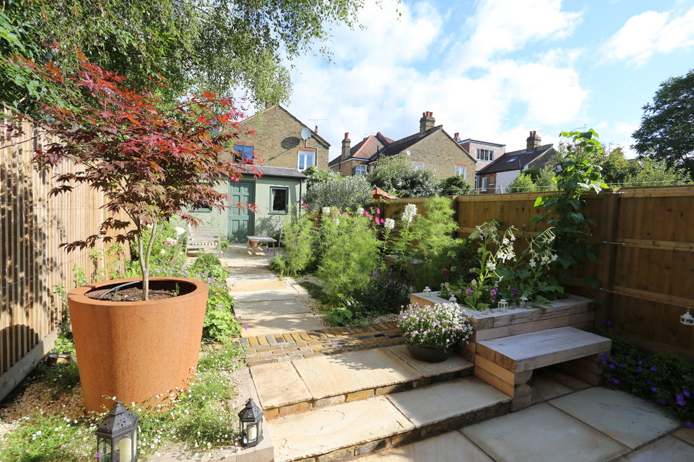 Cette image montre un petit jardin à la française arrière chalet l'été avec une exposition ensoleillée et des pavés en pierre naturelle.