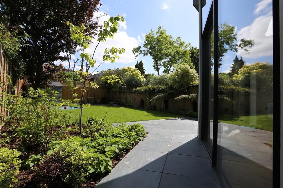 Medium sized modern back formal partial sun garden in London with natural stone paving.