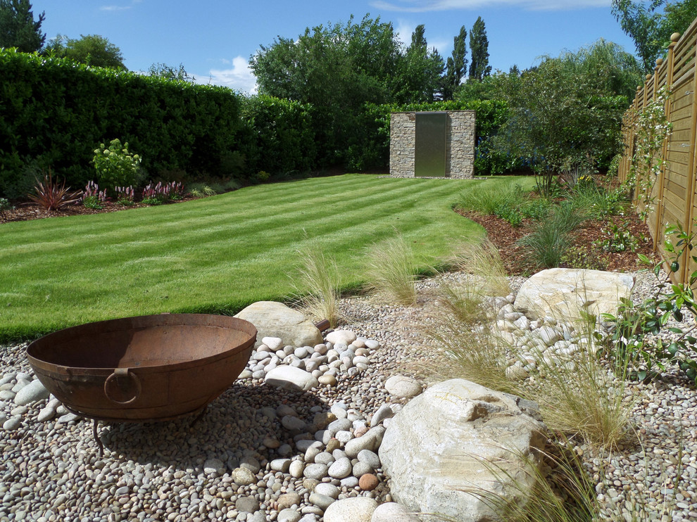 Modelo de jardín actual de tamaño medio en verano en patio trasero con fuente, exposición total al sol y adoquines de piedra natural