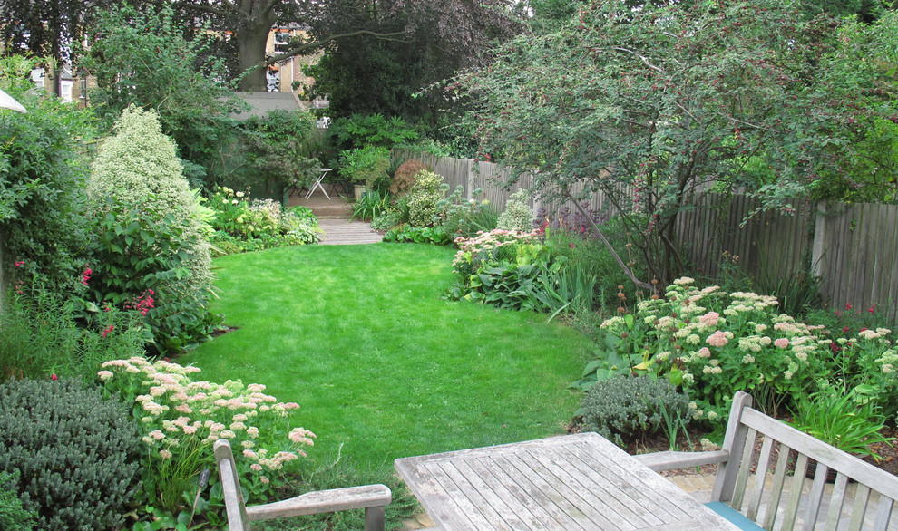 Aménagement d'un grand jardin arrière classique l'été avec une exposition ensoleillée et une terrasse en bois.