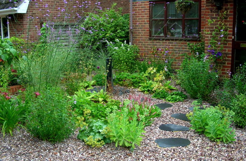 Exempel på en liten uppfart i delvis sol framför huset på sommaren, med en trädgårdsgång och grus