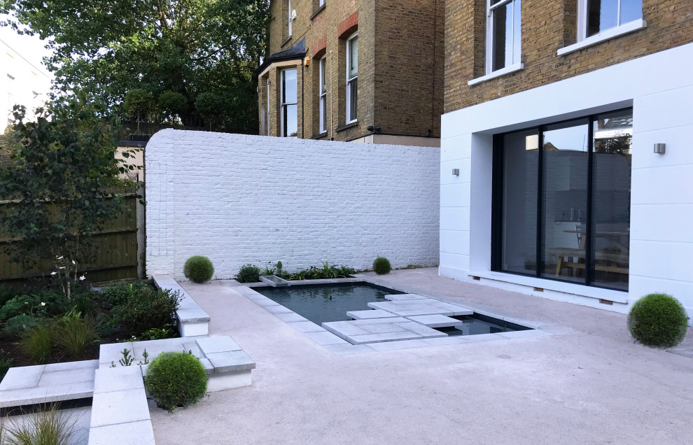Photo of a large contemporary back formal fully shaded garden for autumn in London with a waterfall and natural stone paving.