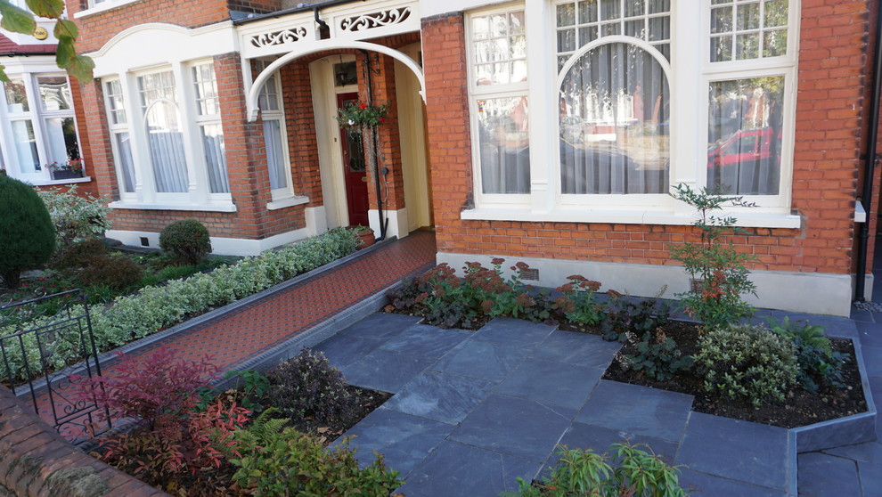 Photo of a small classic front formal partial sun garden for autumn in London with a garden path and natural stone paving.