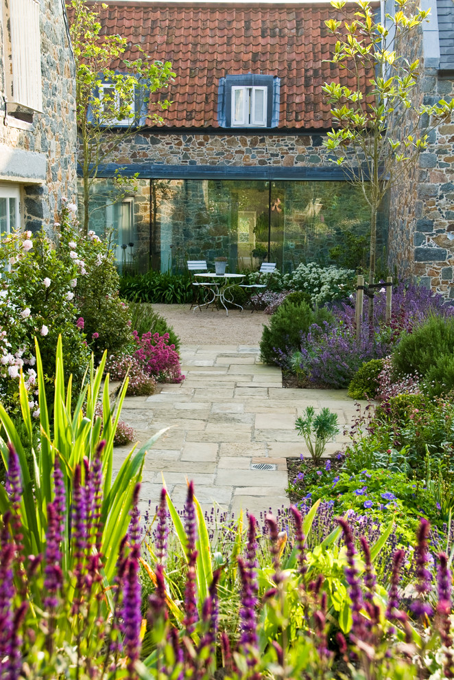This is an example of a large country back full sun garden for summer in Channel Islands with natural stone paving and a garden path.