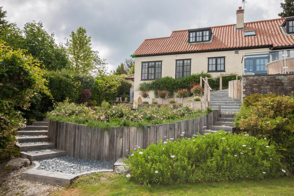 Cette image montre un jardin traditionnel avec un mur de soutènement, une exposition ensoleillée, du gravier et une clôture en bois.