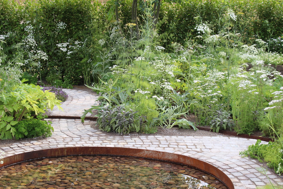 Modelo de jardín de secano campestre pequeño en verano en patio trasero con exposición total al sol, adoquines de piedra natural y estanque