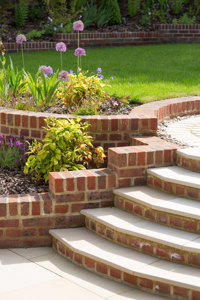 Large traditional sloped formal full sun garden in Cheshire with brick paving.