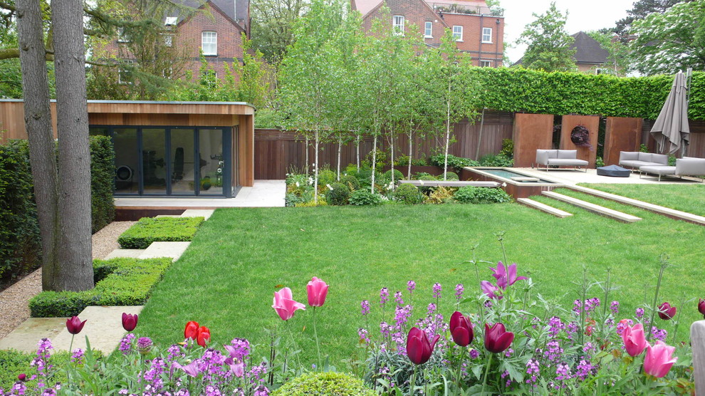 Large contemporary back formal partial sun garden in London with a water feature and natural stone paving.