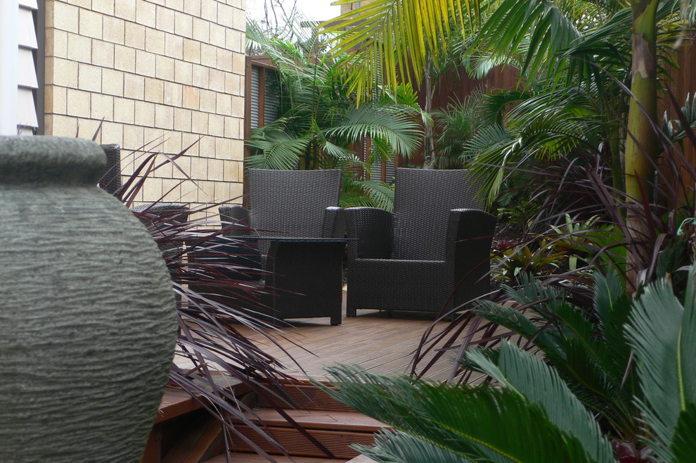 Diseño de jardín tropical pequeño en patio lateral con entablado, fuente y exposición parcial al sol