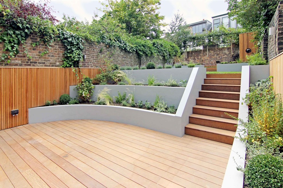 This is an example of a medium sized contemporary back garden in London with a retaining wall and decking.