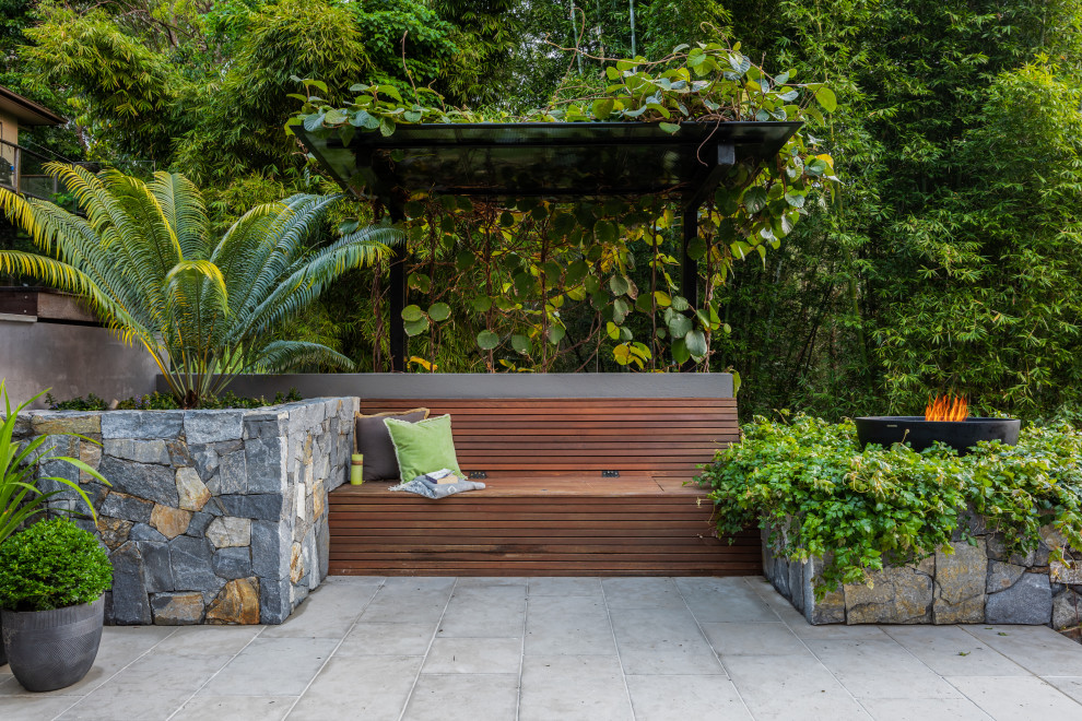Diseño de jardín tropical grande en verano en patio trasero con exposición parcial al sol, adoquines de piedra natural y muro de contención