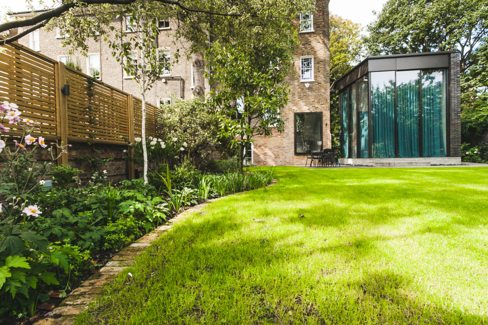 Photo of a mid-sized traditional partial sun backyard brick landscaping in London for summer.