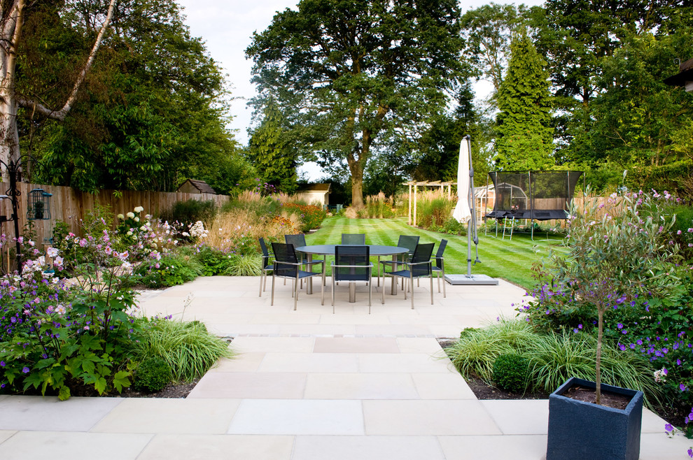Exempel på en stor klassisk trädgård i full sol på sommaren, med en trädgårdsgång och naturstensplattor