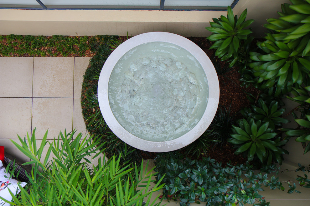 Modelo de jardín tropical pequeño en patio con fuente, exposición reducida al sol y adoquines de piedra natural