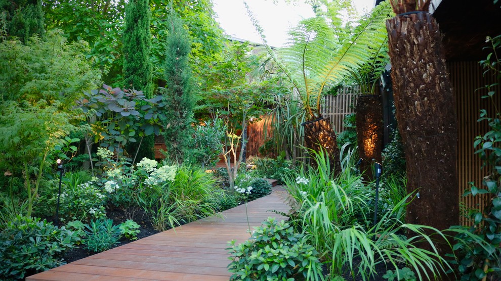 Imagen de jardín tropical grande en patio trasero con exposición parcial al sol y entablado