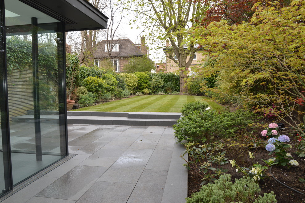 Photo of a large contemporary courtyard formal partial sun garden for spring in London with natural stone paving.