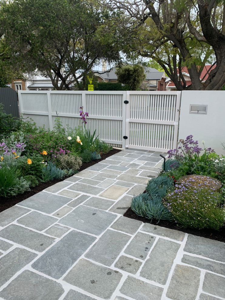 This is an example of a medium sized modern front full sun garden for spring in Adelaide with a garden path, natural stone paving and a wood fence.