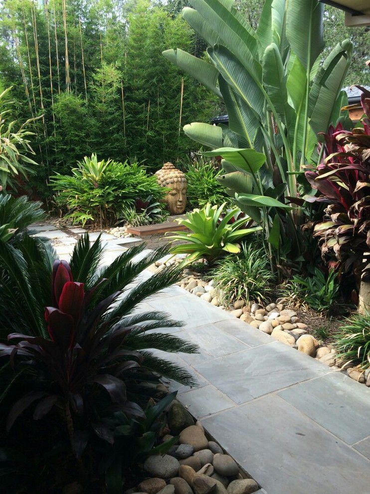 Ejemplo de jardín tropical de tamaño medio en patio trasero con fuente y adoquines de piedra natural