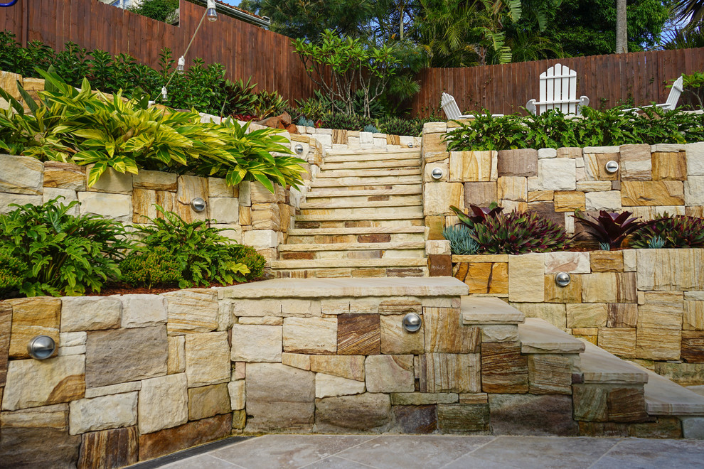 Diseño de jardín costero en patio trasero con muro de contención y adoquines de piedra natural