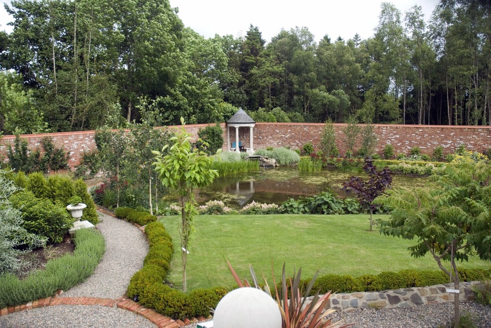 Foto di un ampio giardino formale country esposto in pieno sole dietro casa in estate con fontane e ghiaia