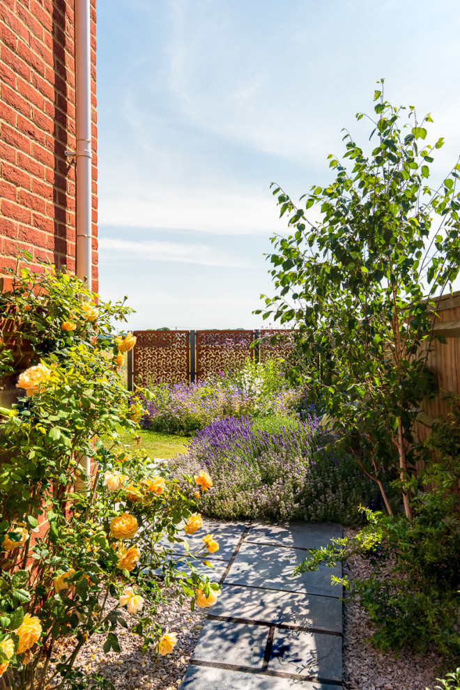 Exempel på en liten lantlig trädgård i delvis sol längs med huset, med en trädgårdsgång och naturstensplattor