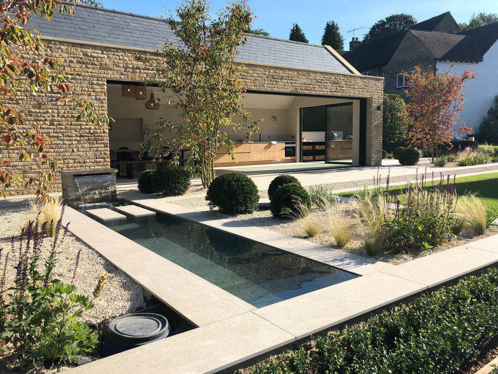 Imagen de jardín actual grande en patio trasero con jardín francés, cascada, exposición parcial al sol y adoquines de piedra natural