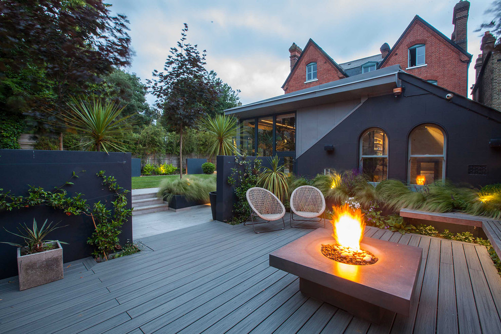 Idée de décoration pour un grand jardin arrière design avec un foyer extérieur et une terrasse en bois.