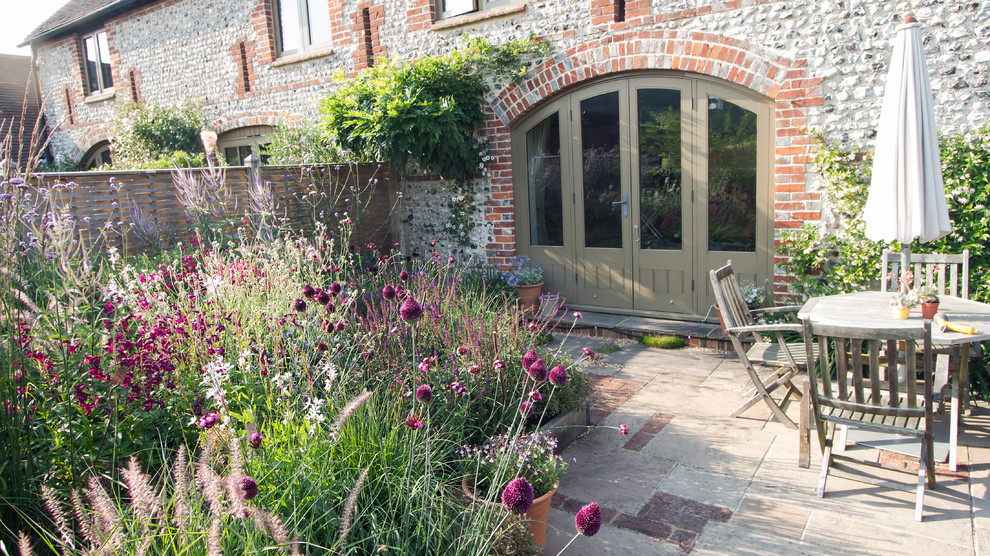 This is an example of a small farmhouse back xeriscape full sun garden for summer in Sussex with natural stone paving.