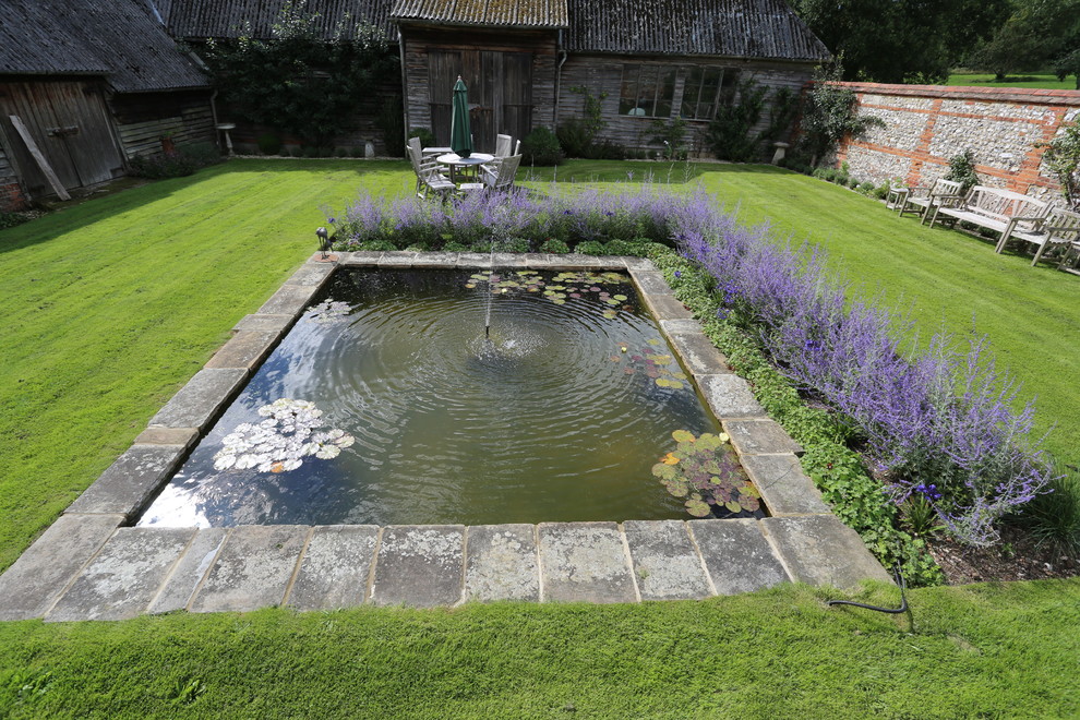 Geometrischer, Großer Country Garten im Sommer, hinter dem Haus mit Wasserspiel, direkter Sonneneinstrahlung und Natursteinplatten in Hampshire