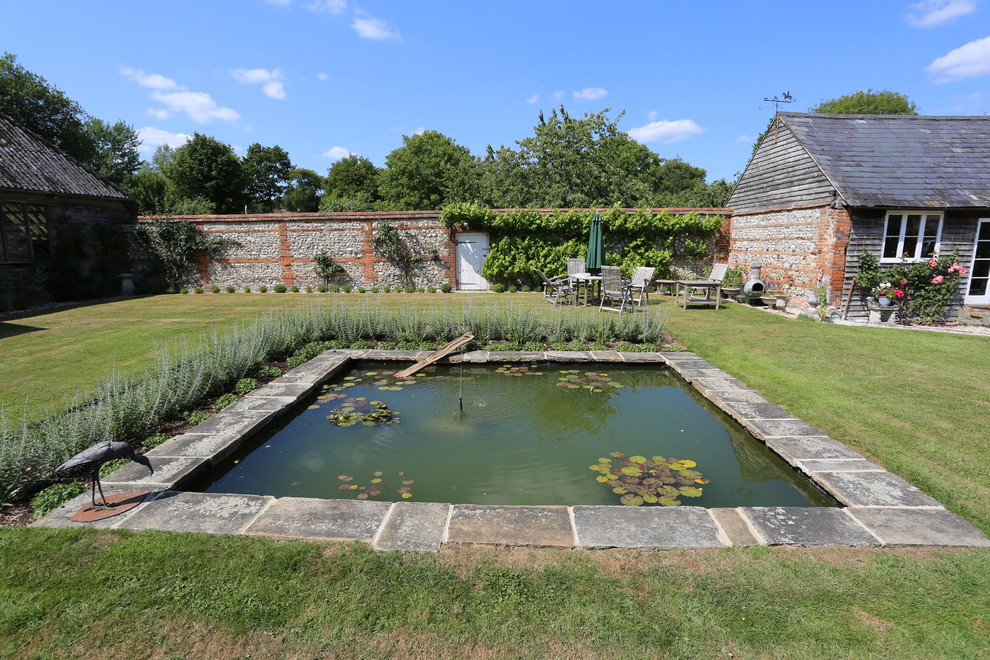 Geometrischer, Großer Landhausstil Garten im Sommer, hinter dem Haus mit Wasserspiel, direkter Sonneneinstrahlung und Natursteinplatten in Hampshire
