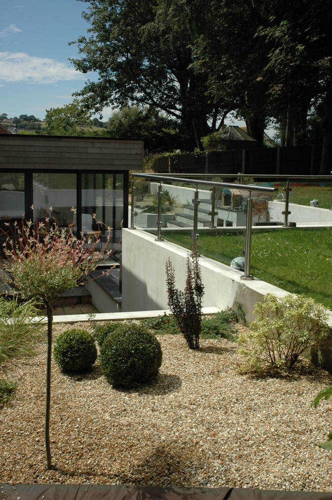 Cette image montre un grand jardin design l'été avec une exposition ensoleillée, du gravier, une pente, une colline ou un talus et un mur de soutènement.