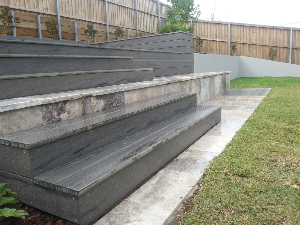 Large contemporary back formal garden in Sydney with a retaining wall and natural stone paving.