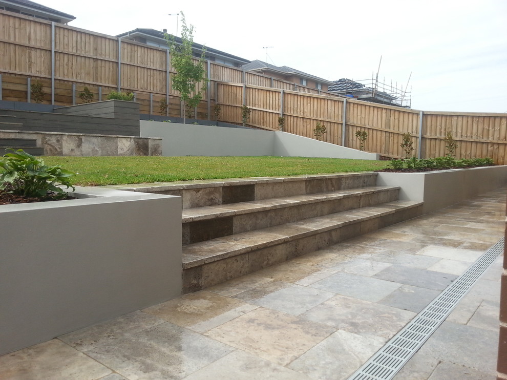 Photo of a large contemporary back formal garden in Sydney with a retaining wall and natural stone paving.