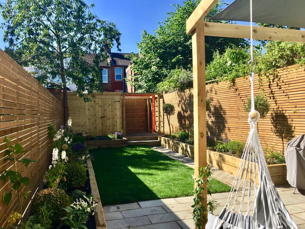 This is an example of a small contemporary back xeriscape partial sun garden for summer in London with a climbing frame and natural stone paving.