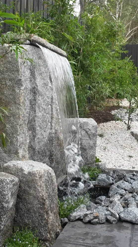 Cette image montre un jardin arrière asiatique avec un point d'eau et des pavés en pierre naturelle.