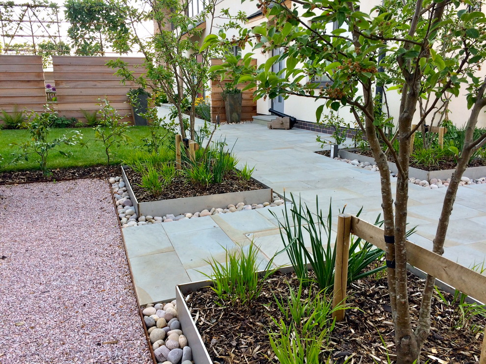 This is an example of a contemporary front formal full sun garden in Devon with a garden path and natural stone paving.