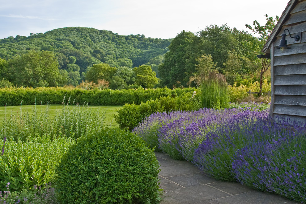 Foto på en stor lantlig bakgård i delvis sol på sommaren, med en trädgårdsgång och naturstensplattor
