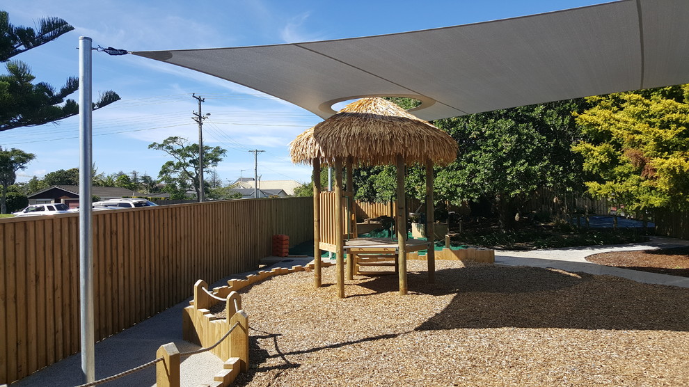 Foto di un giardino tropicale esposto in pieno sole dietro casa con uno spazio giochi