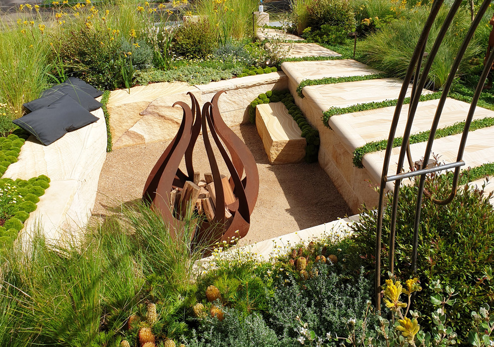 Modelo de jardín de secano industrial de tamaño medio en verano en patio trasero con brasero, exposición total al sol y adoquines de piedra natural