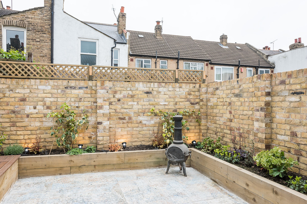 Small contemporary back formal full sun garden for spring in London with a retaining wall and decking.