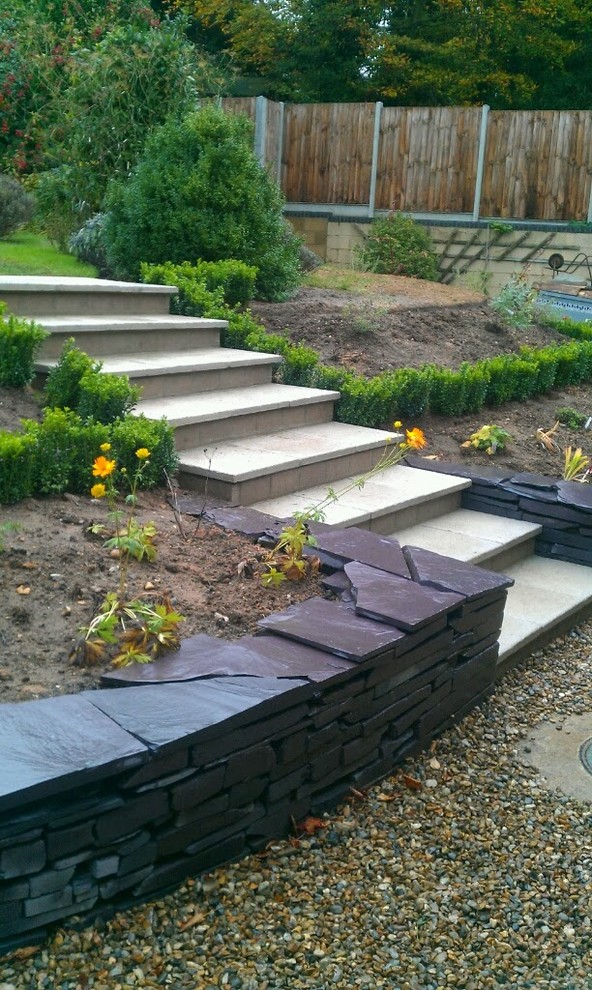 This is an example of a medium sized traditional back formal full sun garden for summer in Other with a retaining wall and natural stone paving.