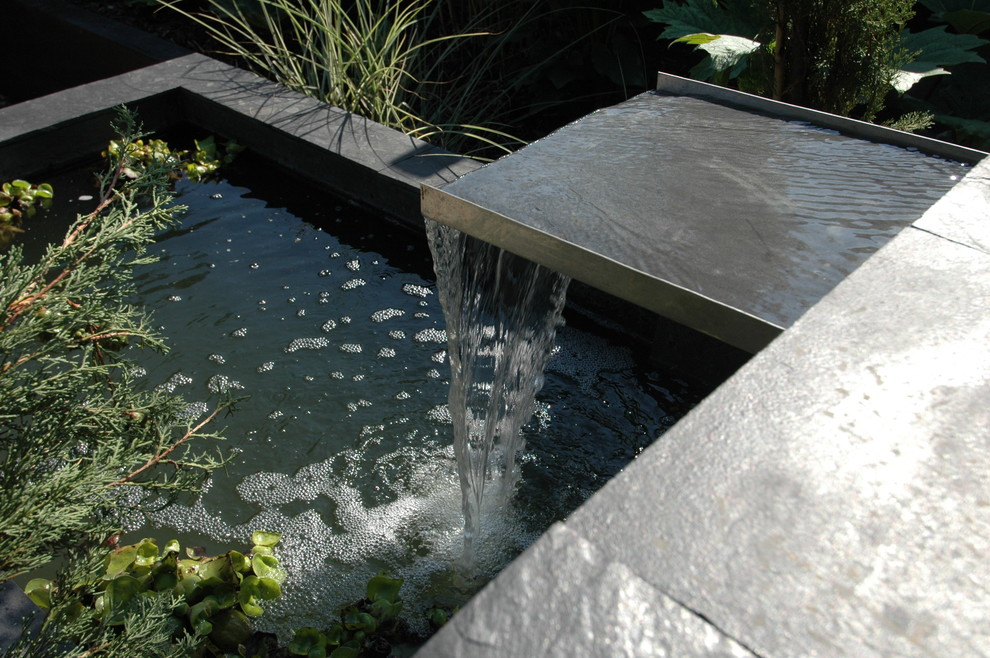 Exempel på en mellanstor modern trädgård i delvis sol, med en fontän och naturstensplattor