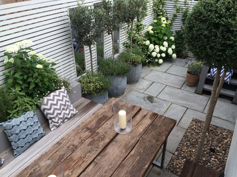 Photo of a small modern back fully shaded garden for summer in London with a potted garden and natural stone paving.