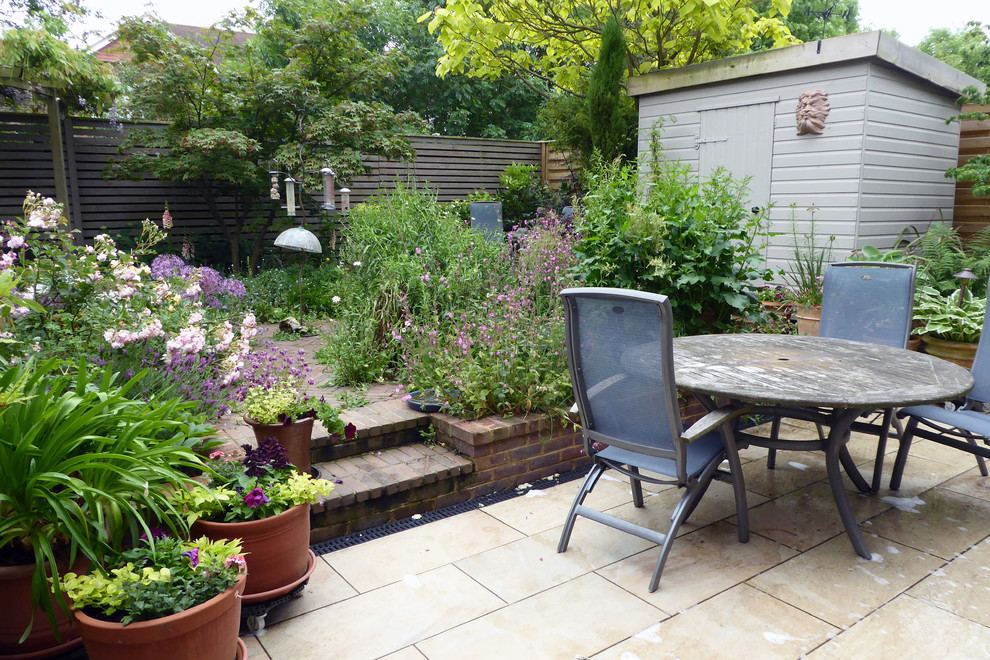 Small contemporary back full sun garden for summer in Hertfordshire with a retaining wall and brick paving.